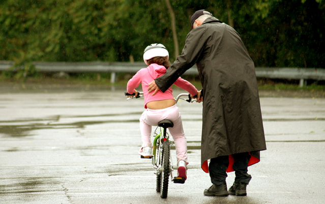 starší muž v plášti učí malou holčičku jezdit na kole